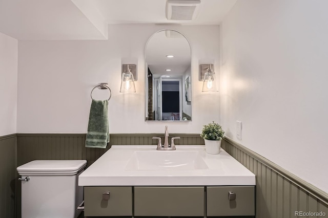 half bathroom with visible vents, a wainscoted wall, toilet, and vanity