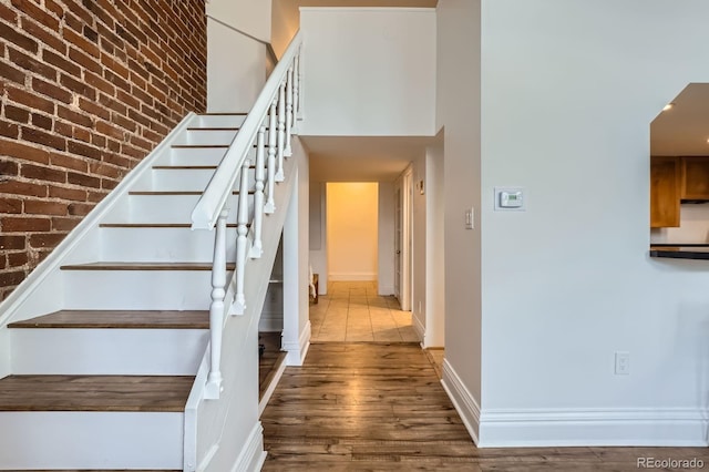 stairs with baseboards, brick wall, and wood finished floors