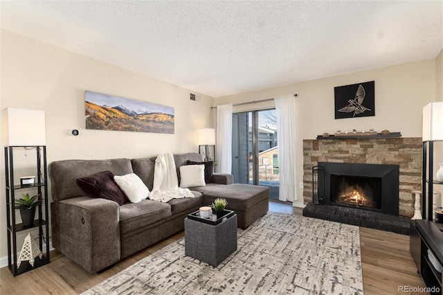 living area with a textured ceiling, a fireplace, visible vents, and wood finished floors