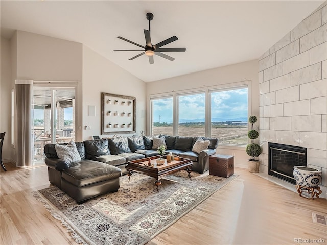 living room with ceiling fan, tile walls, vaulted ceiling, light hardwood / wood-style floors, and a fireplace