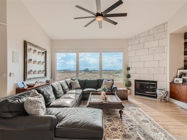 living room with ceiling fan, light wood-type flooring, a tile fireplace, tile walls, and vaulted ceiling