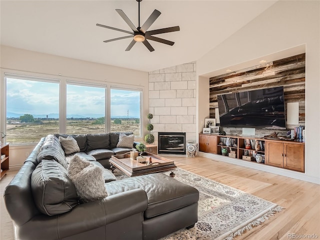 living room with ceiling fan, light wood-type flooring, tile walls, a tiled fireplace, and lofted ceiling