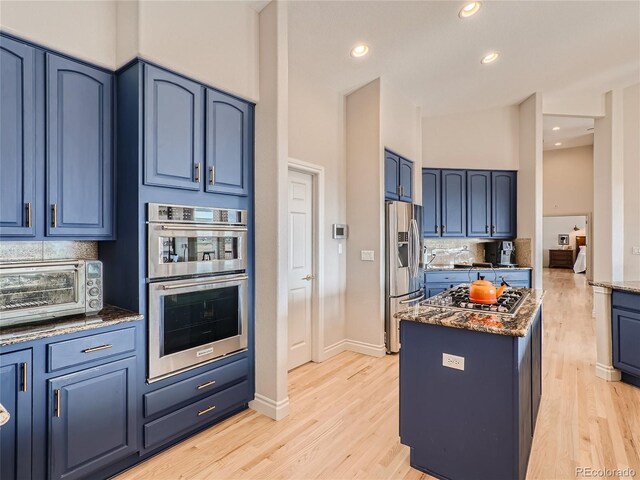 kitchen with dark stone counters, tasteful backsplash, blue cabinets, light hardwood / wood-style floors, and stainless steel appliances