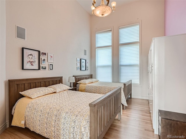 bedroom with a high ceiling, light hardwood / wood-style flooring, and a chandelier