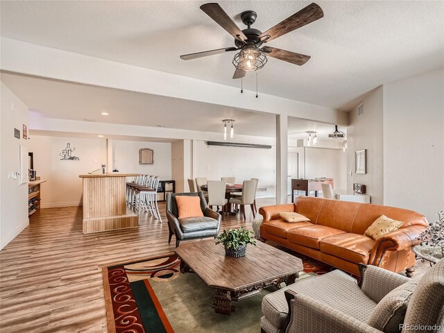 living room with light hardwood / wood-style floors, ceiling fan, and a textured ceiling