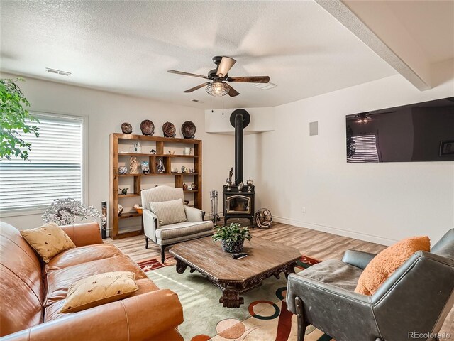 living room featuring ceiling fan, light hardwood / wood-style flooring, a wood stove, and a textured ceiling