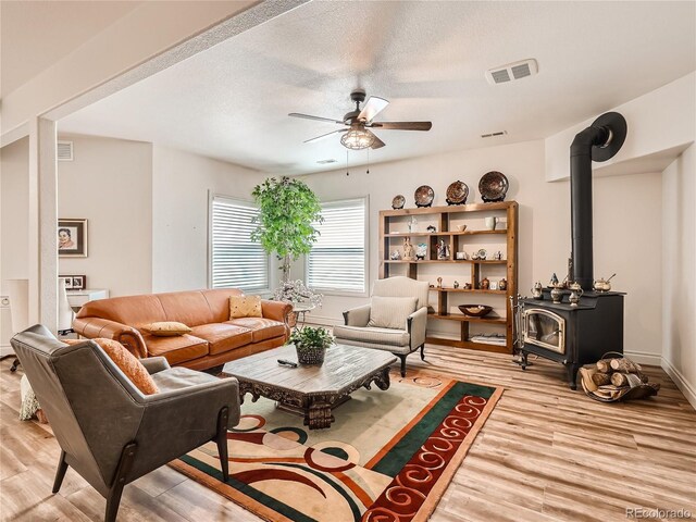 living room featuring light hardwood / wood-style floors, a wood stove, a textured ceiling, and ceiling fan