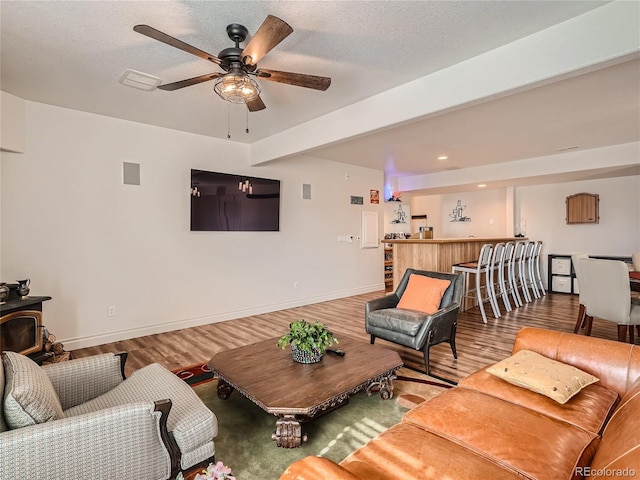 living room with ceiling fan, beamed ceiling, hardwood / wood-style floors, and a wood stove