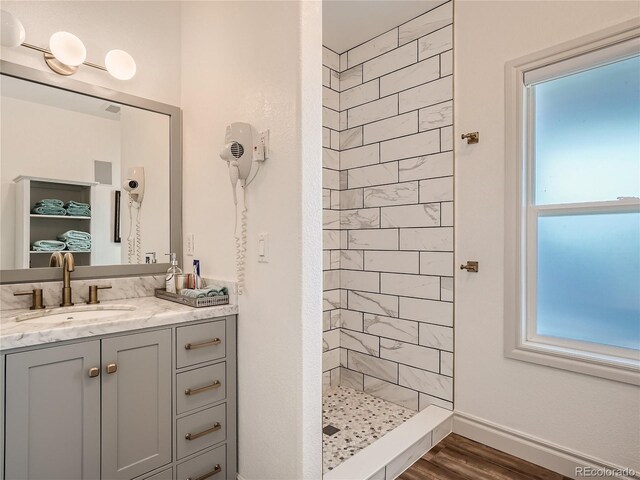 bathroom with wood-type flooring, plenty of natural light, a tile shower, and vanity