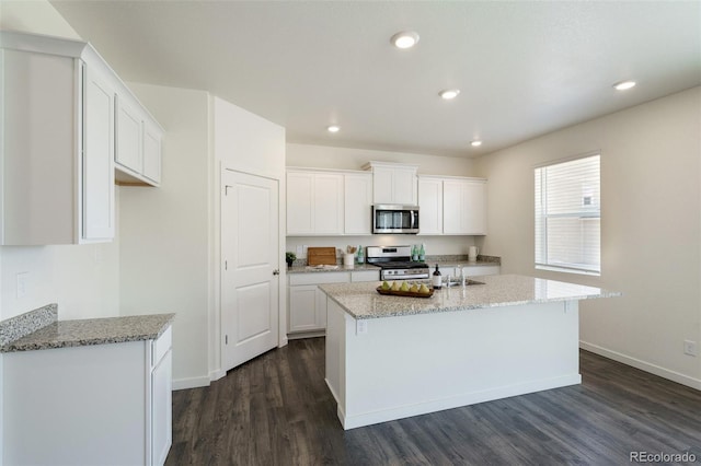 kitchen with white cabinets, appliances with stainless steel finishes, dark hardwood / wood-style floors, and a kitchen island with sink