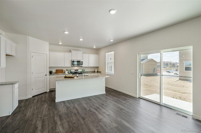 kitchen with dark wood-type flooring, an island with sink, light stone counters, white cabinetry, and stainless steel appliances