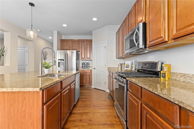 kitchen featuring sink, a kitchen island with sink, stainless steel appliances, light stone countertops, and decorative light fixtures