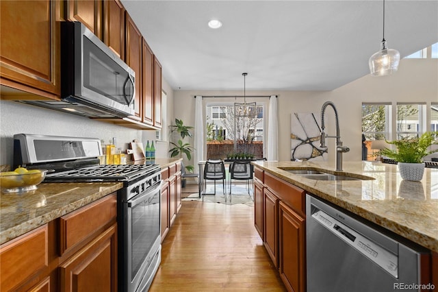 kitchen with light stone counters, stainless steel appliances, decorative light fixtures, and sink