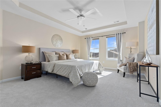 bedroom with ceiling fan, light colored carpet, and a tray ceiling