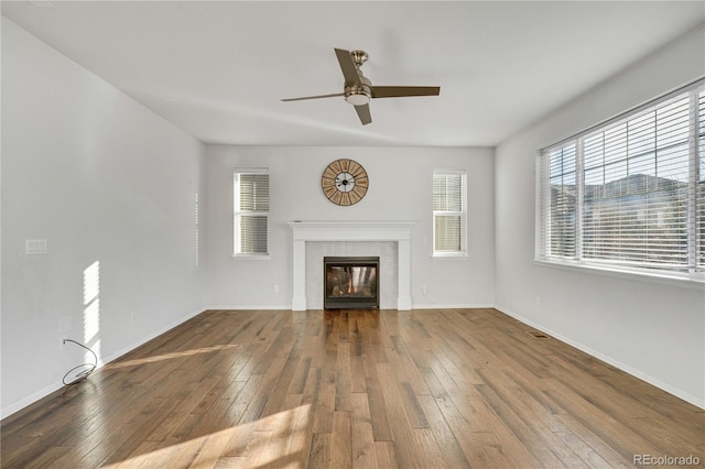 unfurnished living room with a tiled fireplace, ceiling fan, and wood-type flooring