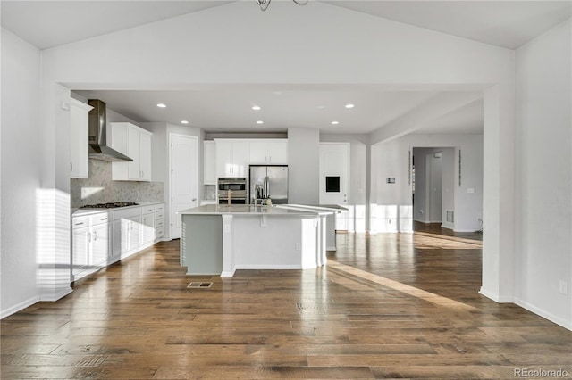 kitchen featuring wall chimney exhaust hood, backsplash, a center island with sink, white cabinets, and appliances with stainless steel finishes