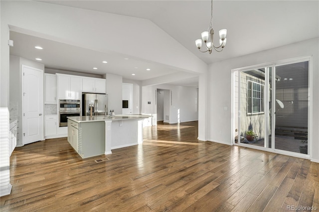 kitchen with white cabinetry, stainless steel appliances, backsplash, an island with sink, and vaulted ceiling