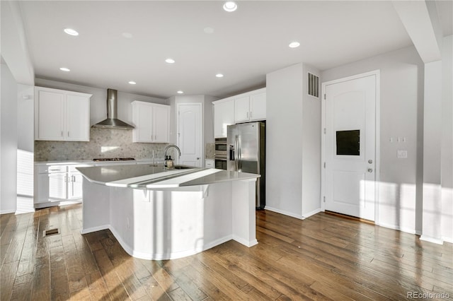 kitchen featuring decorative backsplash, stainless steel fridge with ice dispenser, an island with sink, and wall chimney range hood