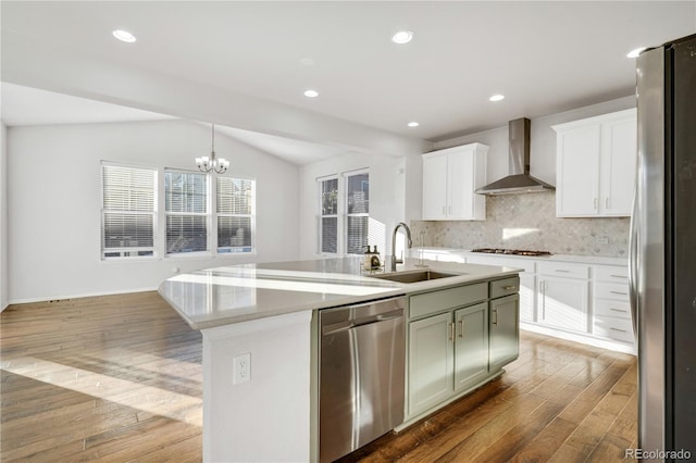 kitchen featuring sink, wall chimney range hood, an island with sink, vaulted ceiling, and appliances with stainless steel finishes