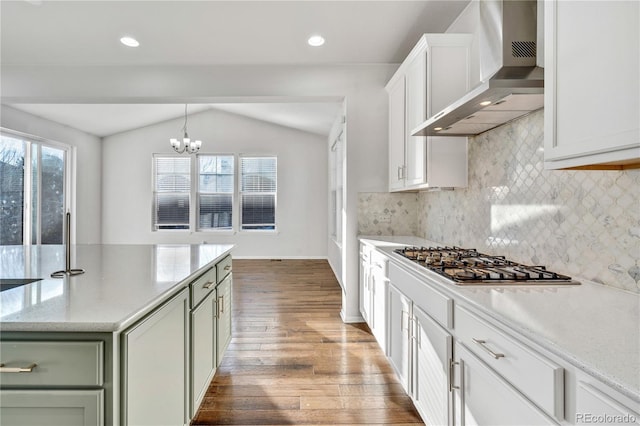 kitchen featuring wall chimney range hood, vaulted ceiling, dark hardwood / wood-style floors, stainless steel gas cooktop, and a chandelier