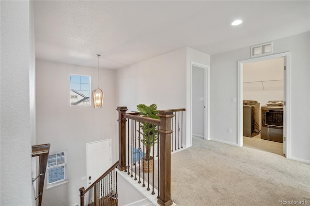 hall featuring light colored carpet, a textured ceiling, and independent washer and dryer