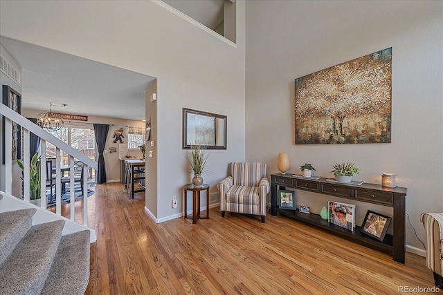 living area with a towering ceiling, light wood-style flooring, an inviting chandelier, baseboards, and stairs