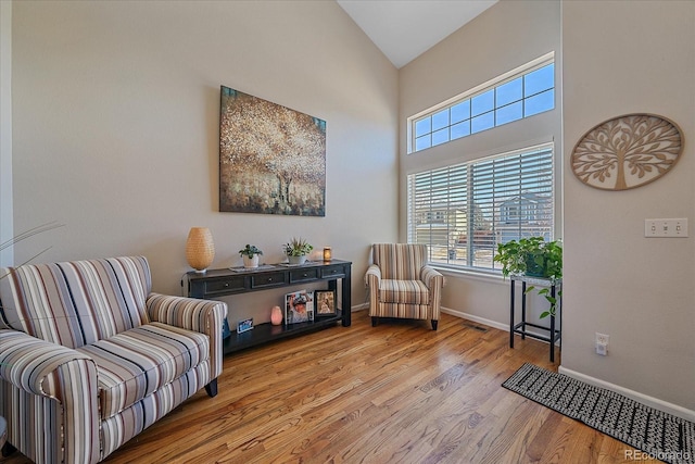 living area with high vaulted ceiling, a wealth of natural light, baseboards, and wood finished floors