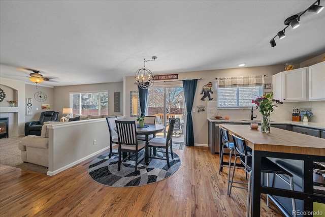 dining area with ceiling fan with notable chandelier, a fireplace, baseboards, light wood-type flooring, and rail lighting