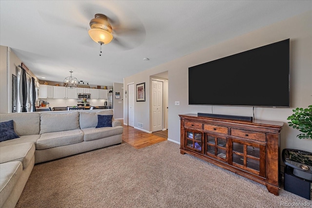 carpeted living area with ceiling fan with notable chandelier and baseboards