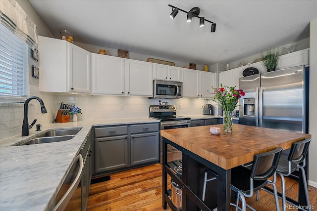 kitchen featuring a sink, wood counters, appliances with stainless steel finishes, light wood-type flooring, and tasteful backsplash