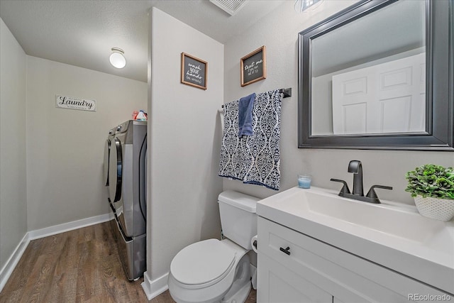 half bath featuring toilet, separate washer and dryer, wood finished floors, vanity, and baseboards