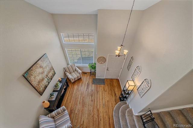 living area featuring a high ceiling, an inviting chandelier, wood finished floors, baseboards, and stairs