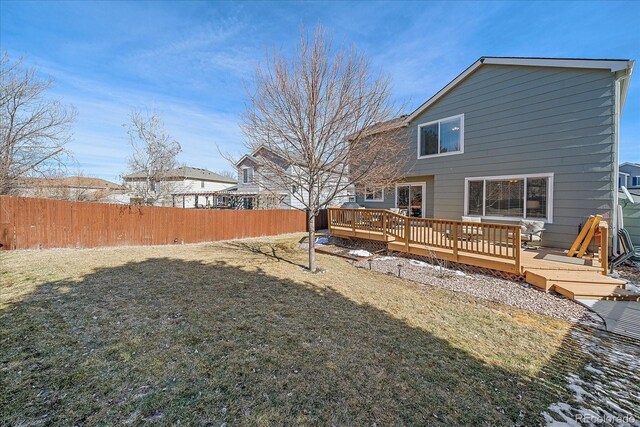 rear view of house featuring fence, a wooden deck, and a lawn