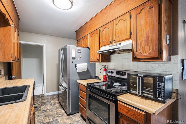547 S 3rd Ave, Brighton, CO 80601 - kitchen with under cabinet range hood, appliances with stainless steel finishes, backsplash, baseboards, and brown cabinetry