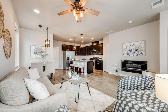 living room with light hardwood / wood-style flooring, ceiling fan, and sink