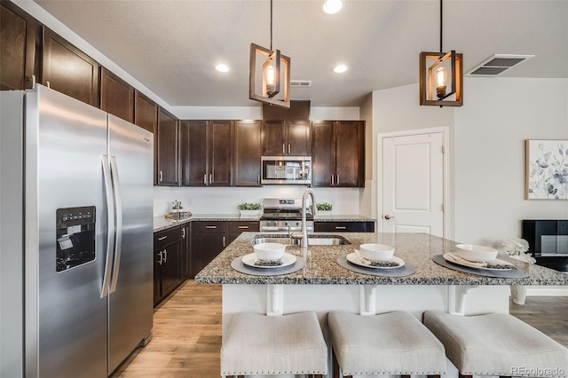 kitchen featuring hanging light fixtures, an island with sink, appliances with stainless steel finishes, and a kitchen bar