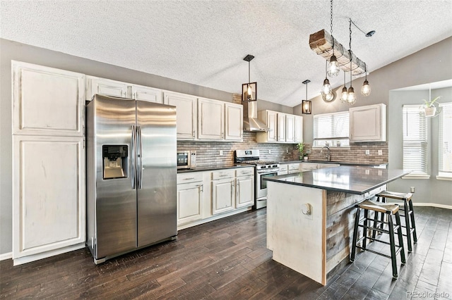 kitchen with a sink, dark countertops, stainless steel appliances, wall chimney exhaust hood, and vaulted ceiling