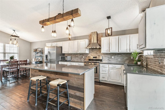 kitchen featuring dark wood-type flooring, wall chimney range hood, vaulted ceiling, appliances with stainless steel finishes, and a sink