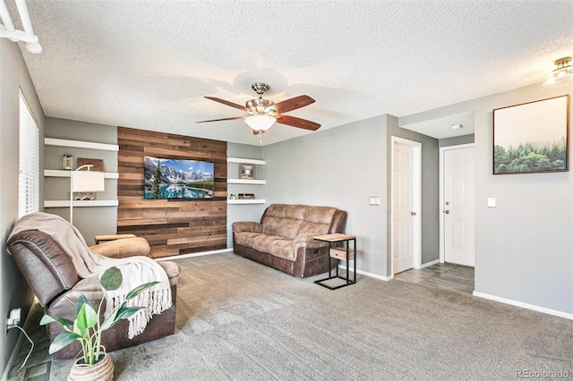 living room featuring baseboards, carpet floors, ceiling fan, wood walls, and a textured ceiling