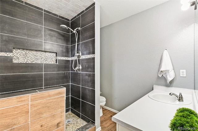 bathroom with toilet, tiled shower, vanity, and wood finished floors