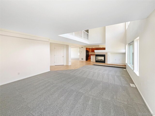 18951 E 43rd Ave, Denver, CO 80249 - unfurnished living room featuring light carpet, visible vents, baseboards, a towering ceiling, and a fireplace