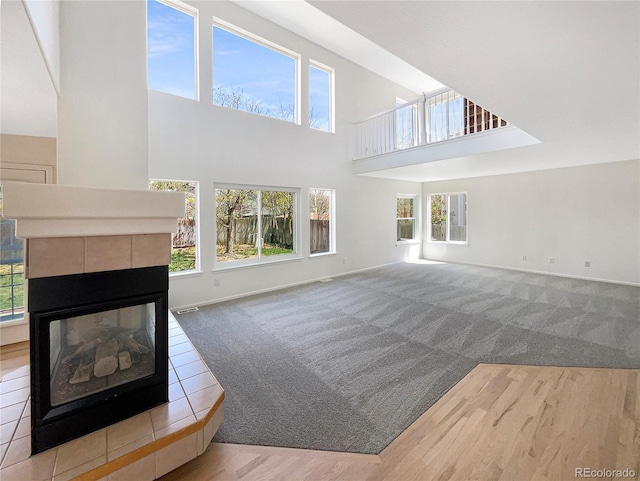 18951 E 43rd Ave, Denver, CO 80249 - unfurnished living room featuring a tiled fireplace, a healthy amount of sunlight, a towering ceiling, and carpet flooring