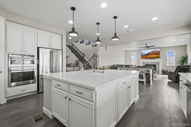 9021 Swan River St, Littleton, CO 80125 - kitchen featuring appliances with stainless steel finishes, a stone fireplace, white cabinetry, dark wood-type flooring, and a ceiling fan