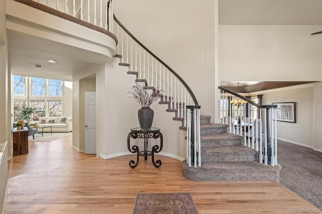 staircase featuring baseboards, a towering ceiling, and wood finished floors