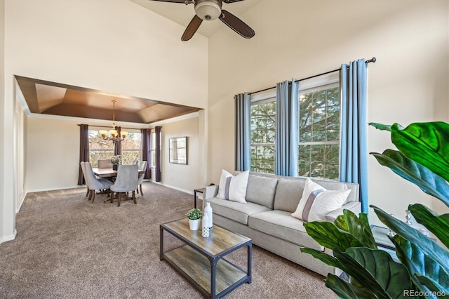 carpeted living area with a raised ceiling, ceiling fan with notable chandelier, a high ceiling, crown molding, and baseboards