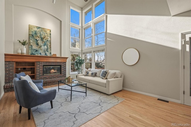 living area featuring visible vents, wood finished floors, a high ceiling, baseboards, and a brick fireplace