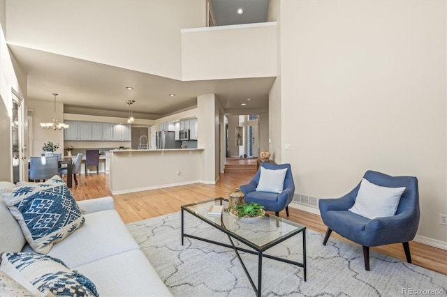 living area with visible vents, baseboards, light wood-style floors, a towering ceiling, and a chandelier