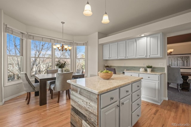 kitchen with light wood finished floors, a kitchen island, light stone countertops, decorative light fixtures, and a notable chandelier