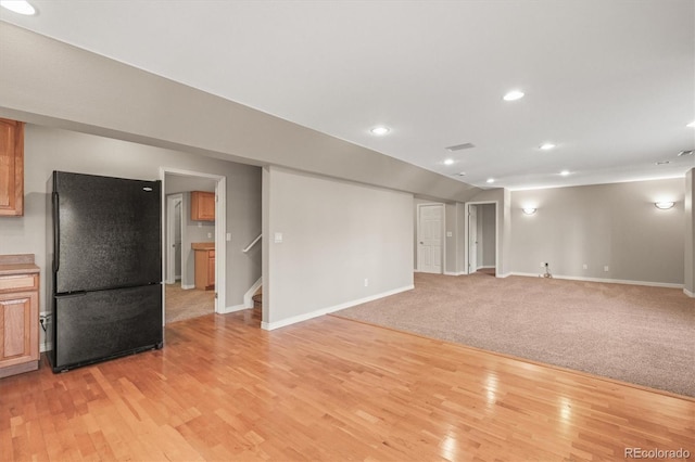 below grade area with stairs, light wood-style flooring, baseboards, and freestanding refrigerator