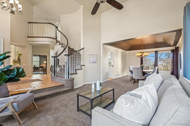 carpeted living area featuring ceiling fan with notable chandelier, visible vents, stairs, a raised ceiling, and baseboards
